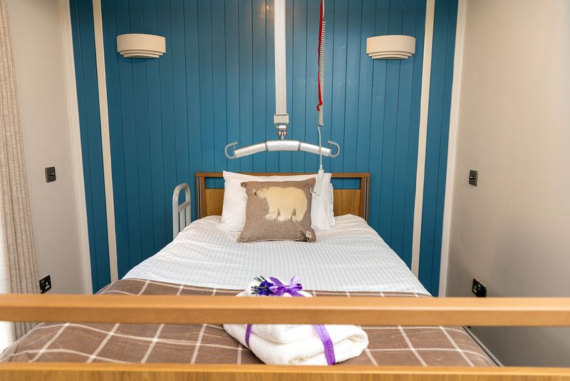 A bed with a polar bear cushion. Towels are tied up with a purple ribbon are at the bottom of the bed.