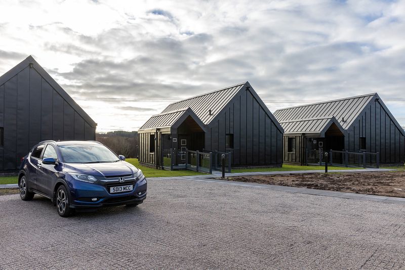 A car is parked on an area of small paving stones behind the chalets.