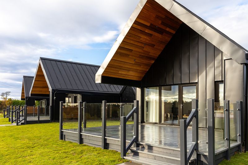 Todhill chalets in the sunshine. They have a black exterior with wide decking and french doors.