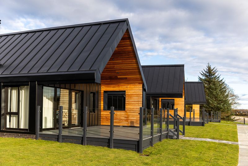 The todhill chalets can be seen from the side, they are on an area of grass with a path in front leading up to steps which go up to the chalet patio.