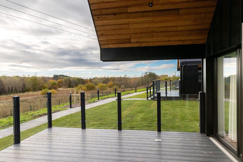 A side view from the modern patio of a Todhill chalet. Beyond can be seen another chalet and a natural scene with different coloured trees in the distance.